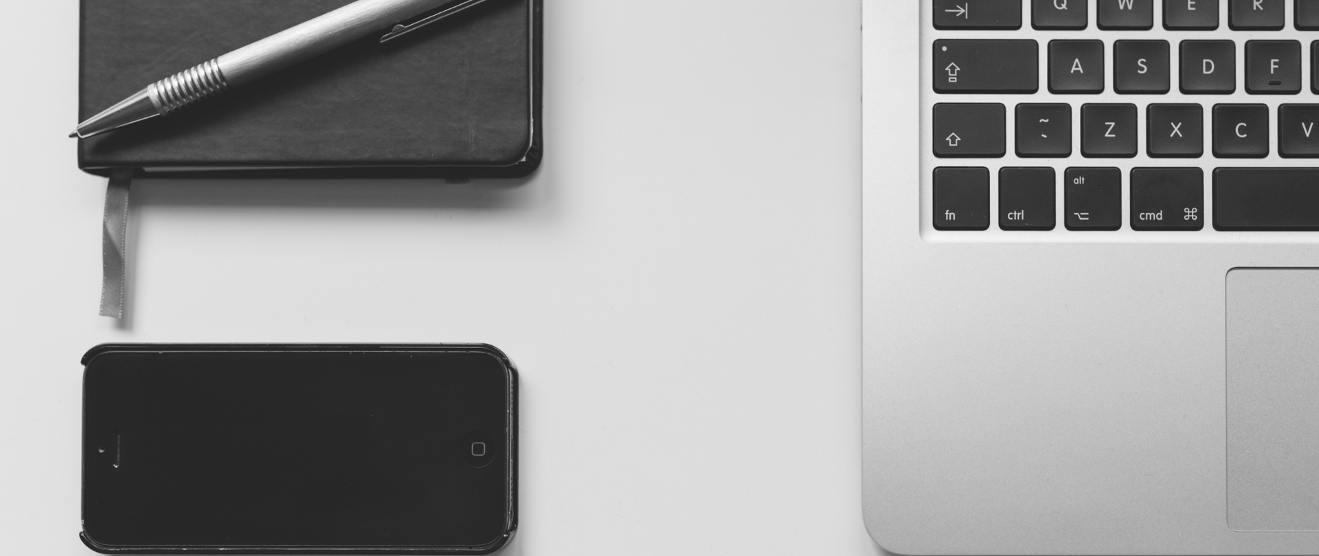 Klawiatura laptopa, obok telefon oraz notes i długopis.