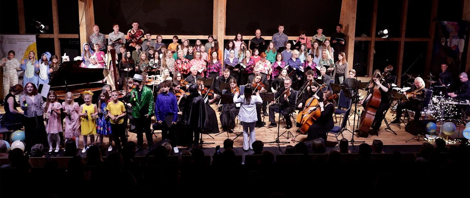 Na zdjęciu orkiestra, chór, soliści, w sumie ok. 60 osób stojących na scenie.