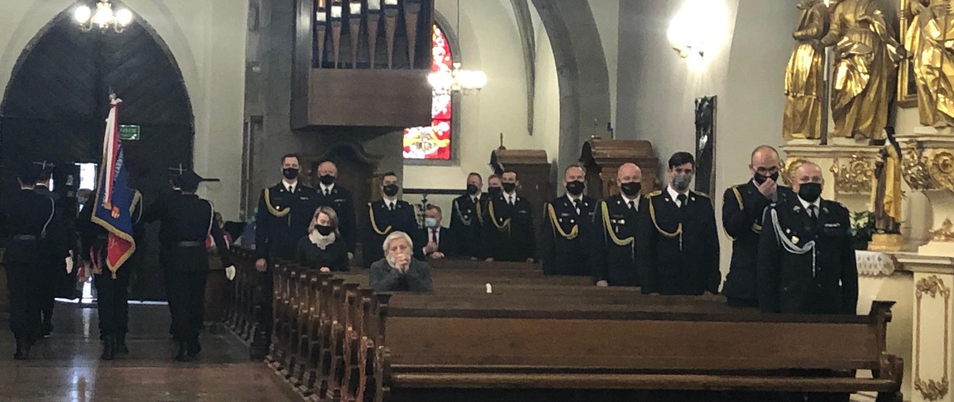 Strażacy uczestniczący w mszy świętej w ławkach. Sztandary wychodzą z bazyliki.