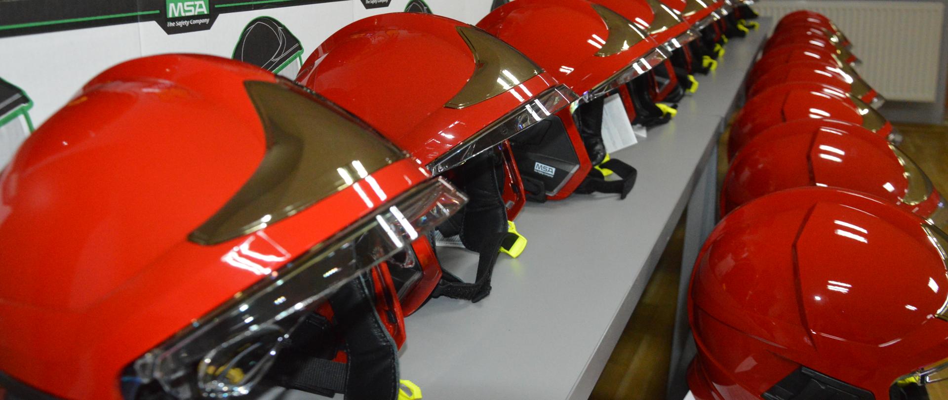 Nowe hełmy strażaków. Świetlica KP PSP w Rawiczu. Na stołach ułożone są nowe hełmy, zakupione dla strażaków JRG. Hełmy maja kolor czerwony.