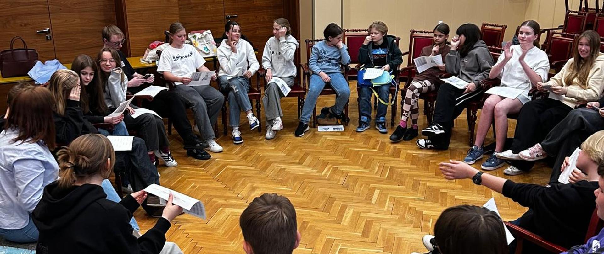 Kobieta i młodzież siedzą na krzesłach w kręgu.