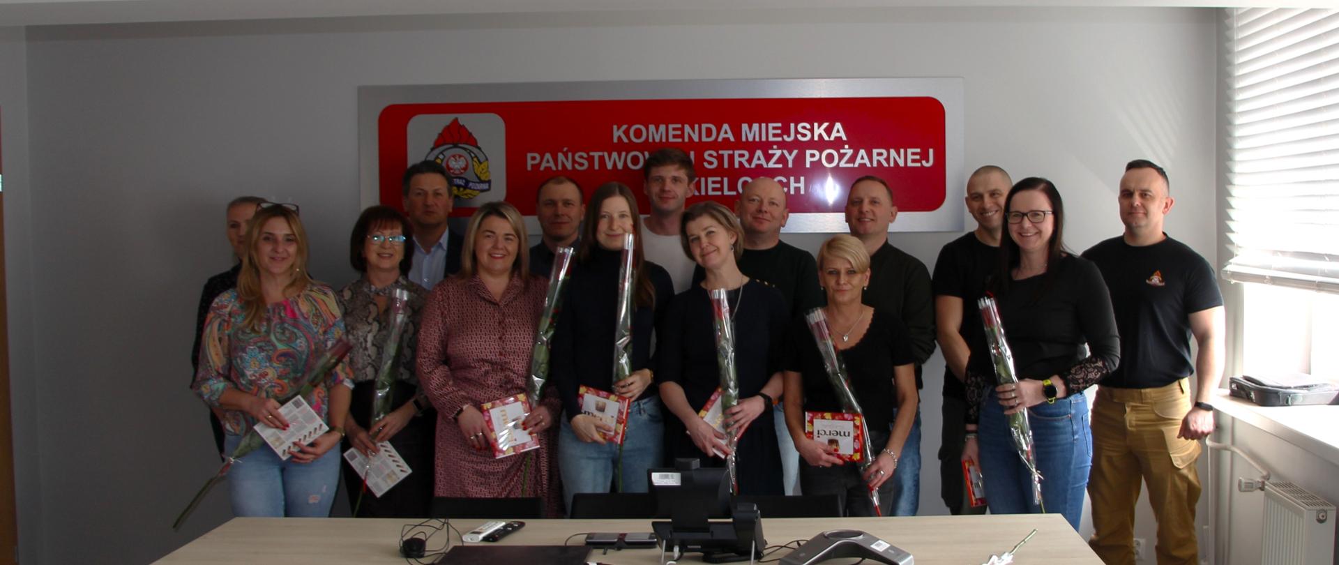 Zdjęcie przedstawia pracowników Komendy Miejskie PSP w Kielcach, Panie stoją trzymając otrzymane kwiaty i słodycze.