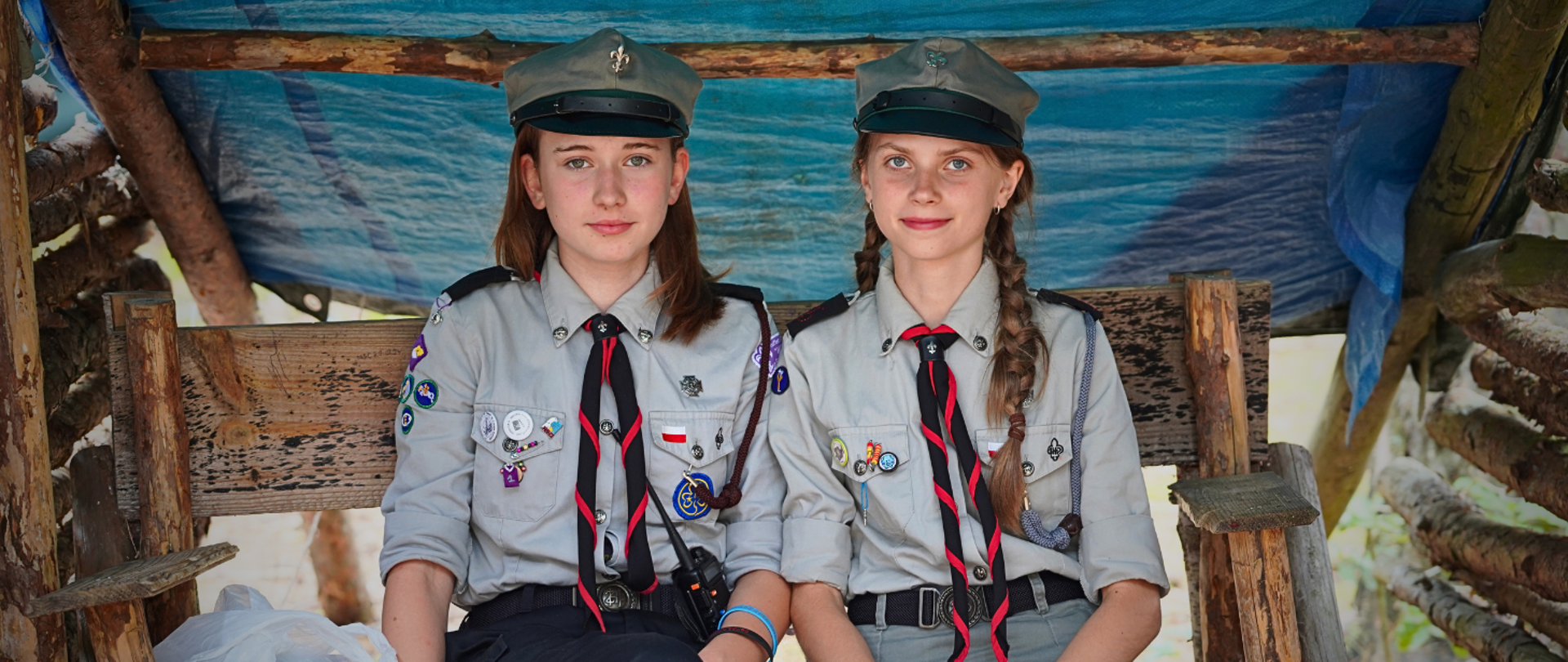 Zdjęcie przedstawia dziewczyny - harcerki, które pełnią wartę w umundurowaniu pod stworzonym namiotem.