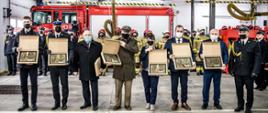 Widoczni przedstawiciele rządu, komendy wojewódzkiej psp, leśnicy, komendant powiatowy psp, przedsiębiorcy, przedstawiciele samorządów, którzy otrzymali grawertony, w tle strażacy w garażu jednostki