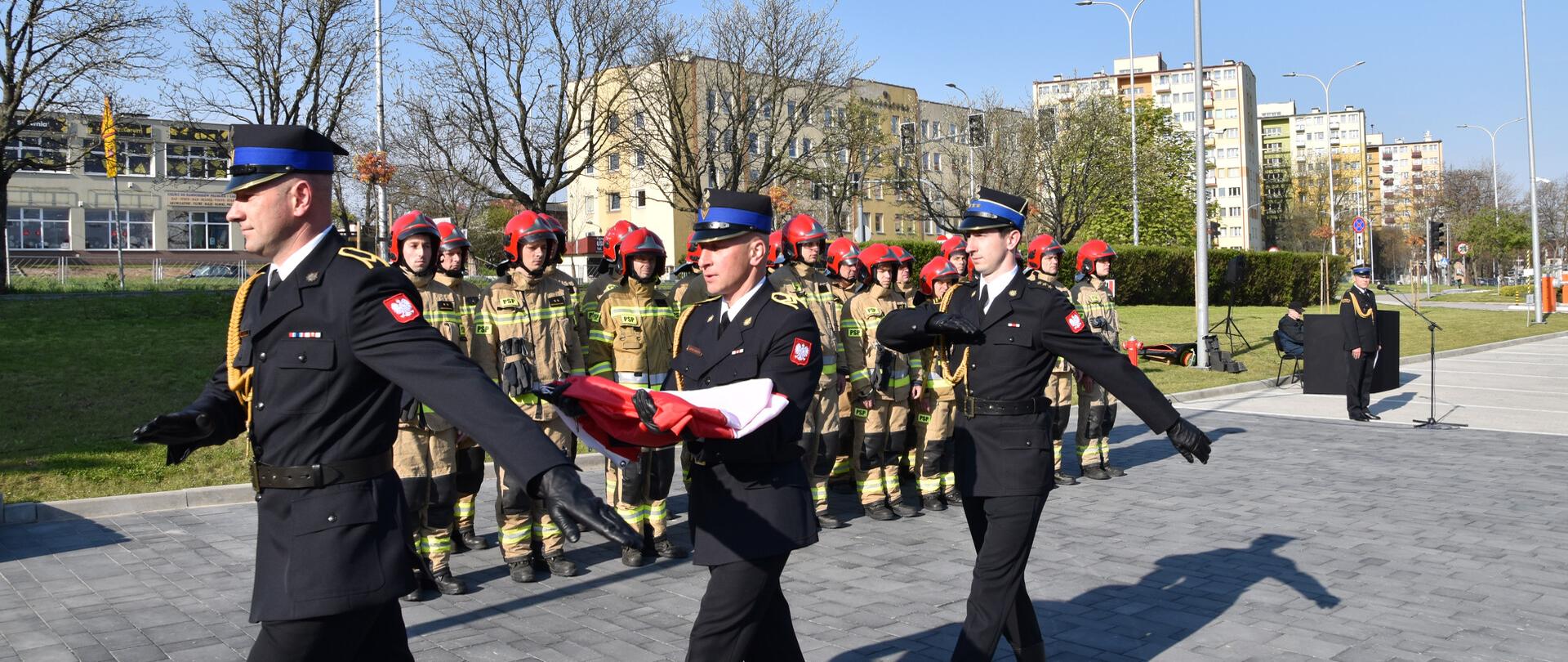 Fotografia przedstawia strażaków Jednostki Ratowniczo-Gaśniczej nr 1 w Kielcach podczas uroczystego podnoszenia biało-czerwonej flagi na maszt .
