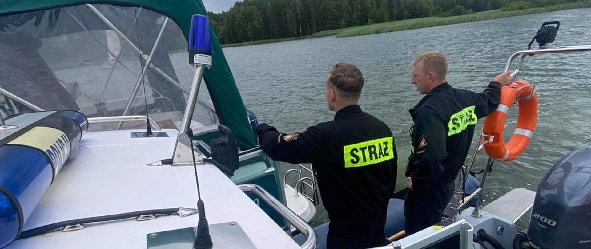 Strażacy patrolujący łodzią akwen wodny.