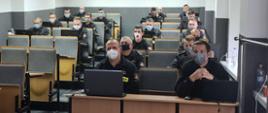 Zdjęcie przedstawia uczestników szkolenia. Szkolenie odbywało się w sali wykładowej. Uczestnicy siedzą po dwie osoby przy jednej ławce. Każdy strażak posiada laptop. Z uwagi na pandemie strażacy mają zakładane maseczki.