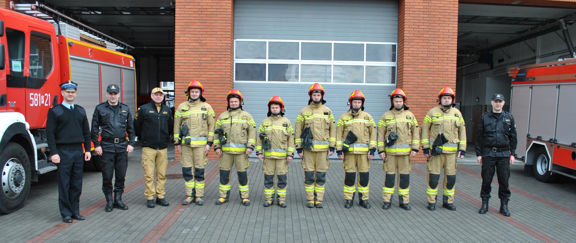Zdjęcie przedstawia Zastępcę Komendanta Głównego PSP oraz kierownictwo Komendy Powiatowej PSP w Słupcy wraz z załogą pomiędzy nimi samochody pożarnicze, na tle budynku komendy .