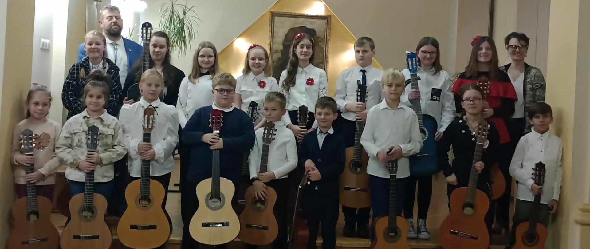 Zdjęcie grupowe wszystkich uczniów klasy gitary wraz nauczycielami A. Kozakowska i W. Kozakowskim, podczas koncertu w auli PSM w Kłodzku