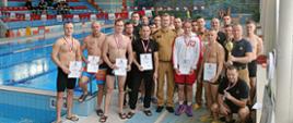 Na zdjęciu przy basenie sportowym ustawieni do zdjęcia wszyscy zawodnicy, którzy brali udział w zawodach w pływaniu, Komendant Miejski Państwowej Straży pożarnej w Częstochowie i jego zastępca oraz sędziowie zawodów.