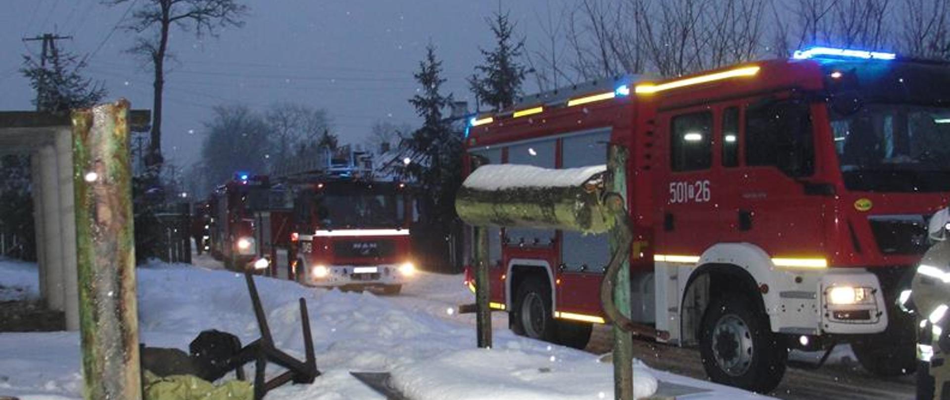 Pojazdy ratowniczo-gaśnicze ustawione przed budynkiem w którym doszło do pożaru kotłowni. Pojazdy maja włączone oświetlenie zewnętrze i niebieskie lampy błyskowe