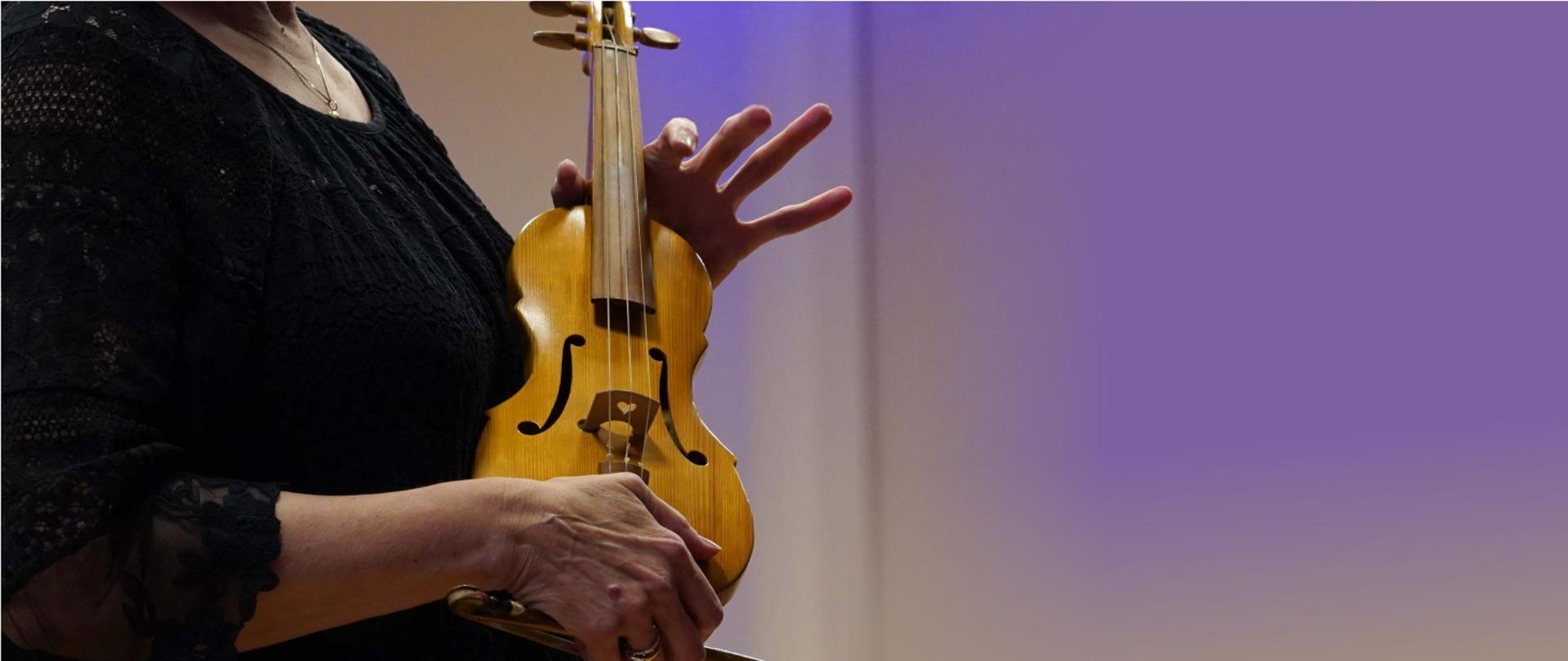 Zdjęcie przedstawia skrzypce barokowe trzymane w rękach skrzypaczki