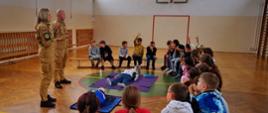 Strażacy przeprowadzają dla dzieci zajęcia edukacyjne na sali gimnastycznej.