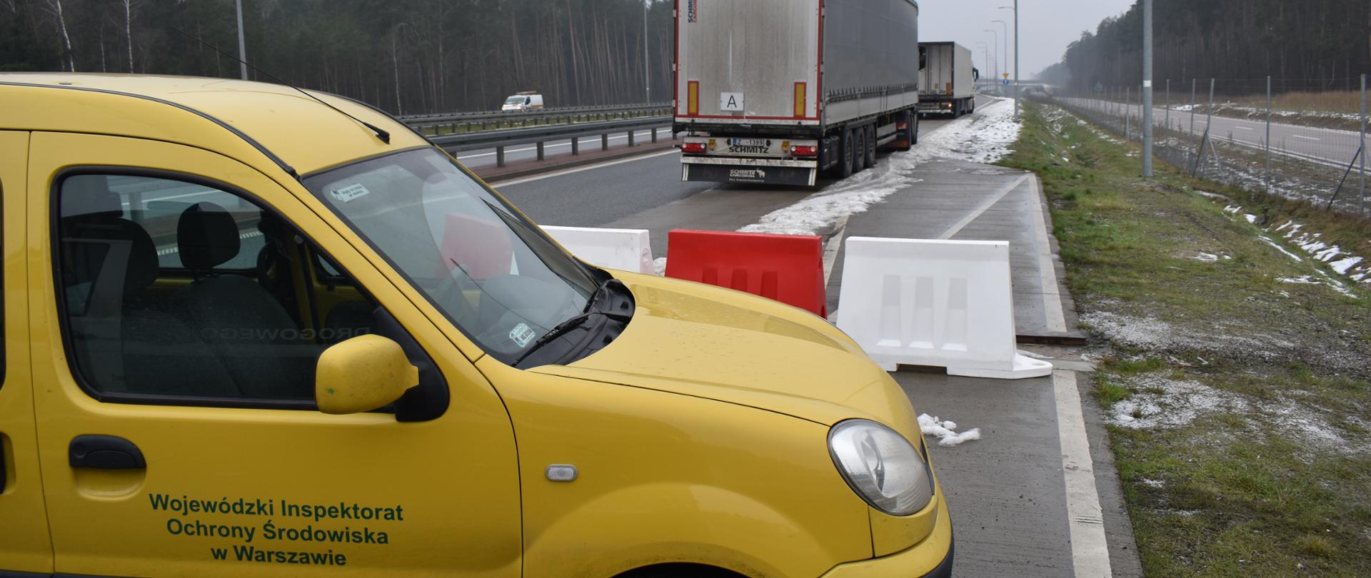 Samochód Wojewódzkiego Inspektoratu Ochrony Środowiska w Warszawie zaparkowany w miejscu przeprowadzania kontroli drogowej. W tle stojące samochody ciężarowe podlegające kontroli.