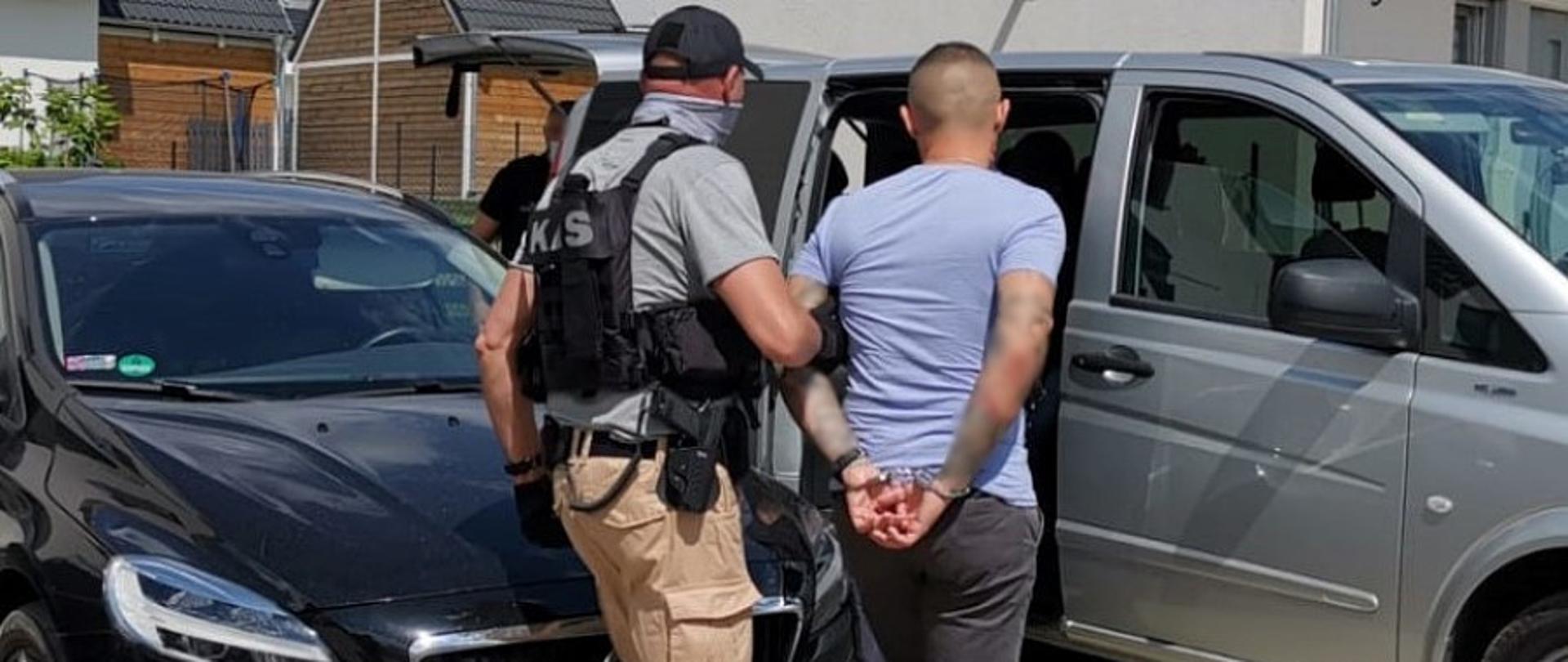 Funkcjonariusz Służby Celno-Skarbowej KAS prowadzi zatrzymanego do samochodu.