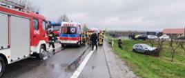 Zdjęcie –dwa ambulanse, samochód pożarniczy , samochód biorący udział w zdarzeniu na a także strażaków oraz policjantów pracujących na miejscu zdarzenia.