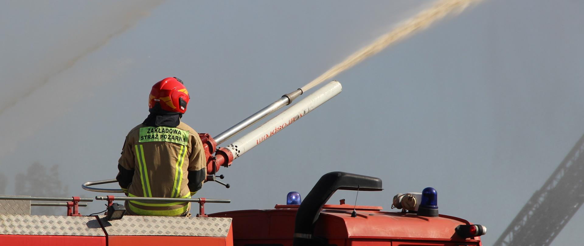 Zdjęcie przedstawia samochód bojowy w trakcie podawania środka gaśniczego z działka samochodowego.
