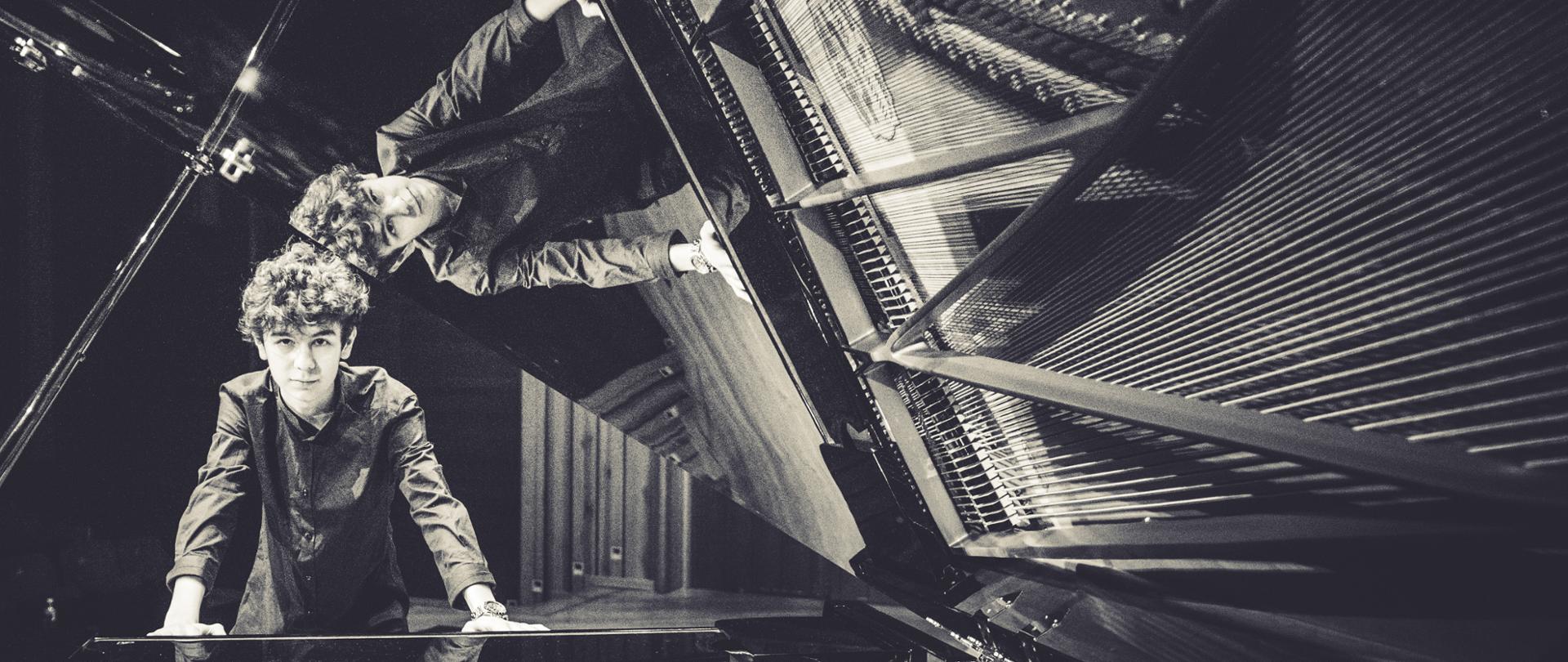 czarnobiałe zdjęcie Mateusza Dubiela przy klawiaturze fortepianu na sali koncertowej ZPSM