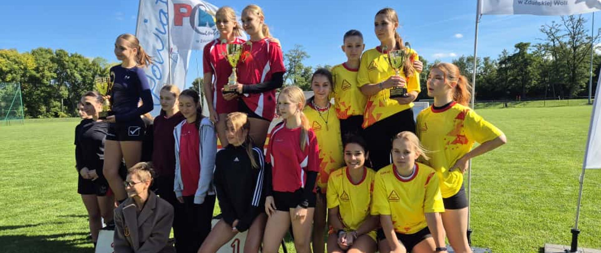 Trzy drużyny prezentujące puchary na tle murawy