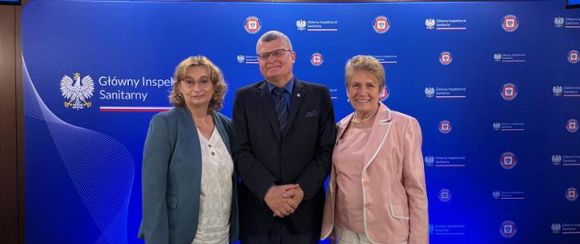 Osoby ustawione do zdjęcia na tle niebieskiej ścianki promocyjnej