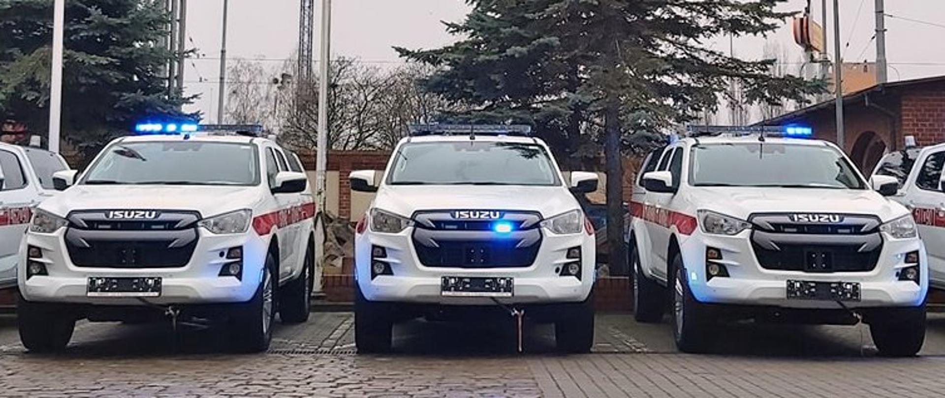 Białe samochody z włączonymi sygnałami z napisem ISUZU