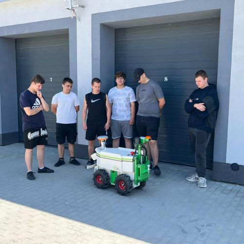 Grupa uczniów obserwuje autonomiczny robot rolniczy podczas prezentacji na placu szkoleniowym.