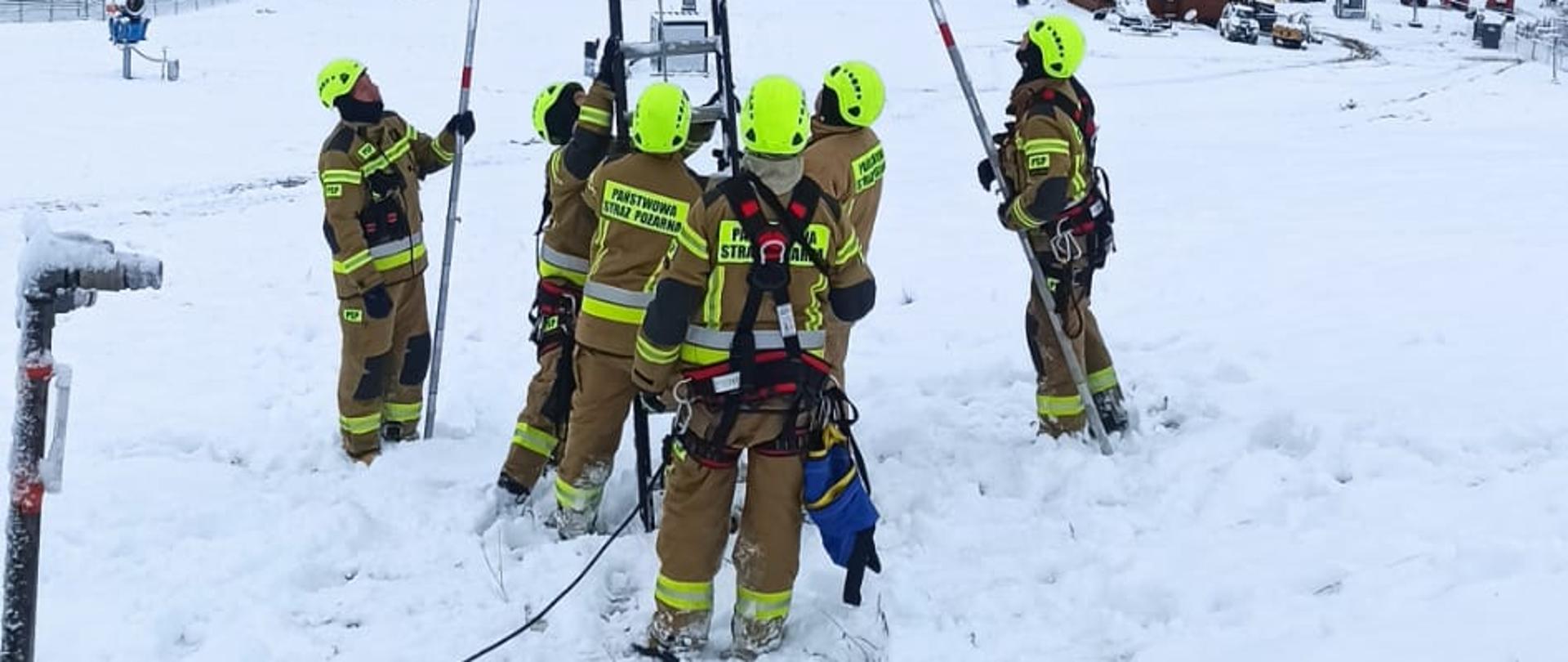 Na zdjęciu widać strażaków w ubraniach specjalnych którzy rozkładają drabinę wysuwną przy wyciągu krzesełkowym. Jedna osoba siedzi na krzesełku.