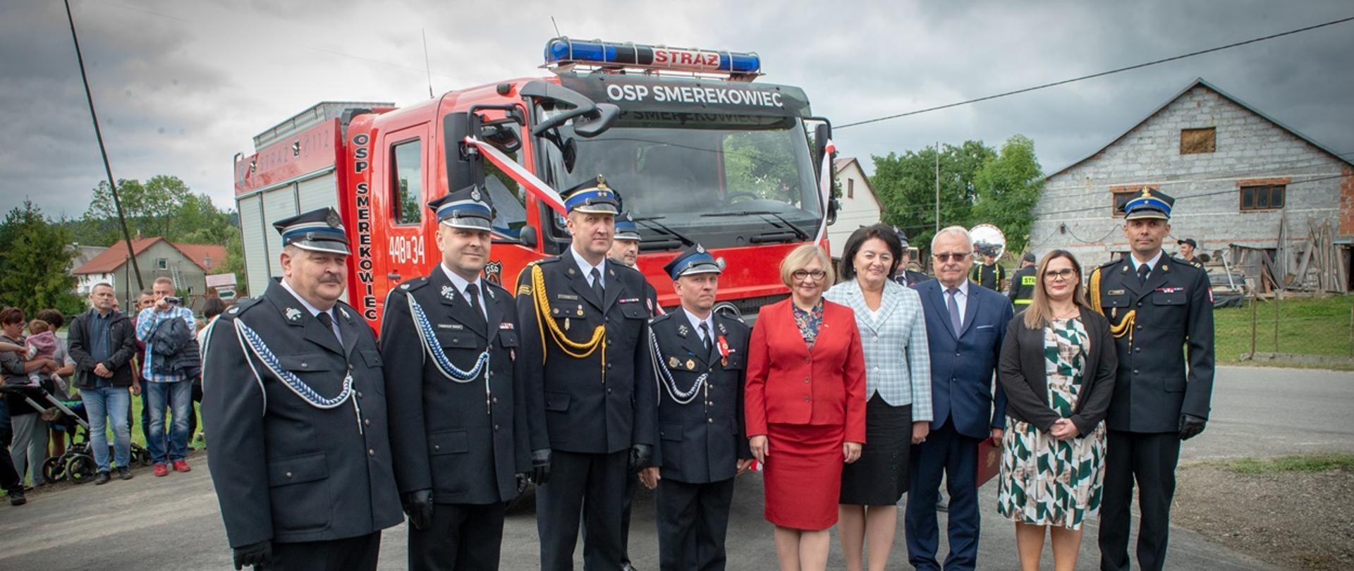 Na zdjęciu w tle widoczny samochód ratowniczo-gaśniczego przekazany podczas uroczystego apelu dla OSP Smerekowiec a przed samochodem strażacy PSP i OSP w galowych mundurach, Pani poseł i samorządowcy 