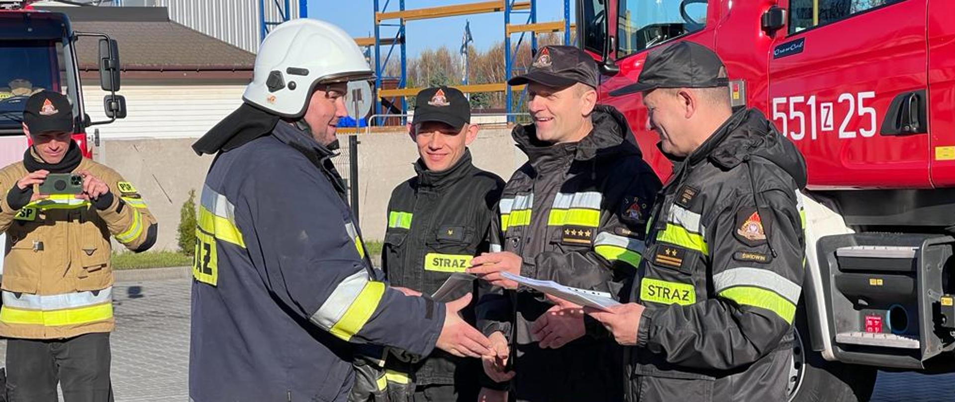 Na zdjęciu widać strażaków Komendy Powiatowej Państwowej Straży Pożarnej którzy, gratulują oraz wręczają certyfikat ukończenia szkolenia strażakowi OSP.