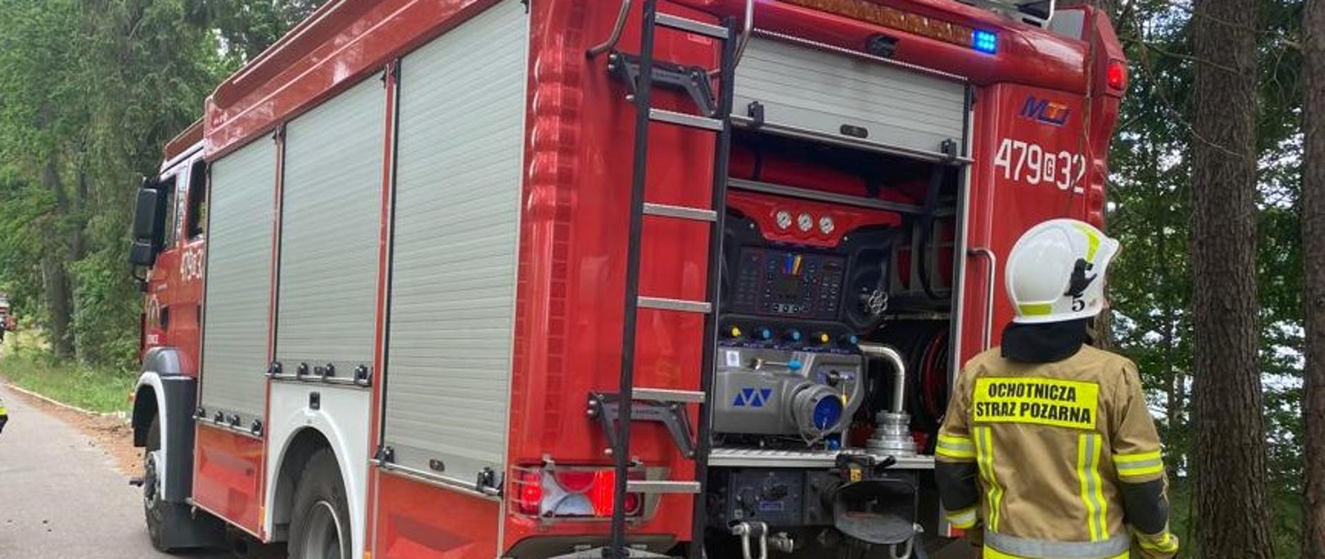 Samochód ratowniczo - gaśniczy, z tyłu stoi strażak OSP w mundurze