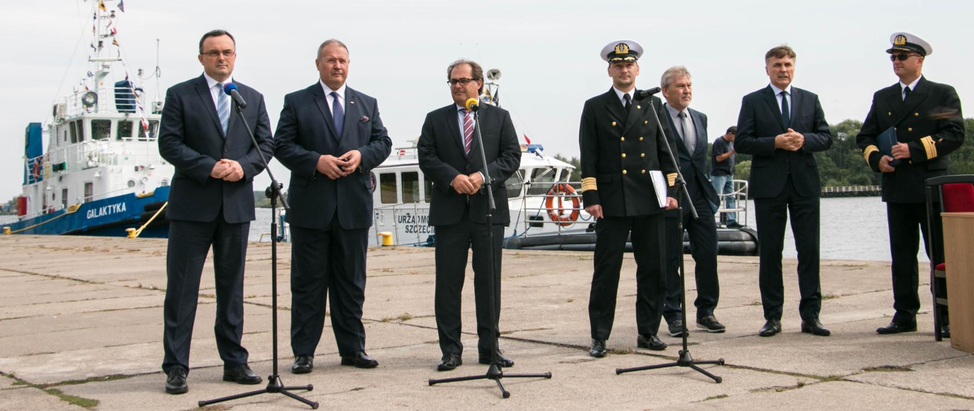 Uczestnicy konferencji prasowej stają przy mikrofonach na nabrzeżu przy torze wodnym w Szczecinie.