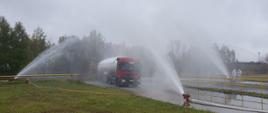 Samochód ciężarowy - cysterna stoi w środku, na samochód podawana jest woda w postaci rozproszonej, z działek wodnych.