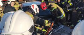 Zdjęcie przedstawia strażaków podczas próby podnoszenia rozcinania elementów karoserii samochodu z użyciem narzędzi hydraulicznych