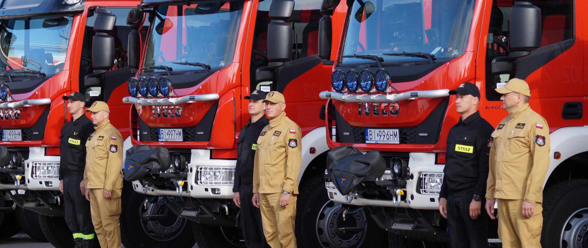 Na zdjęciu widać nowy samochód ratowniczo gaśniczy. Obok samochodów stoją strażacy.