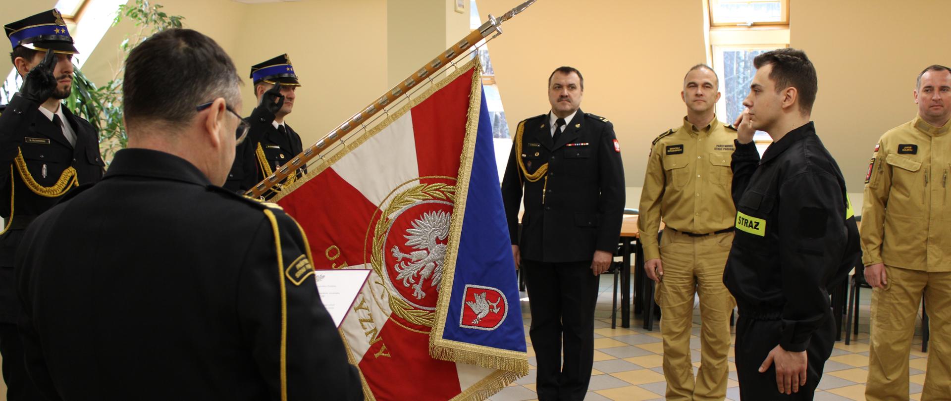 Strażak Igor Kuciński stoi przed sztandarem składa ślubowanie.