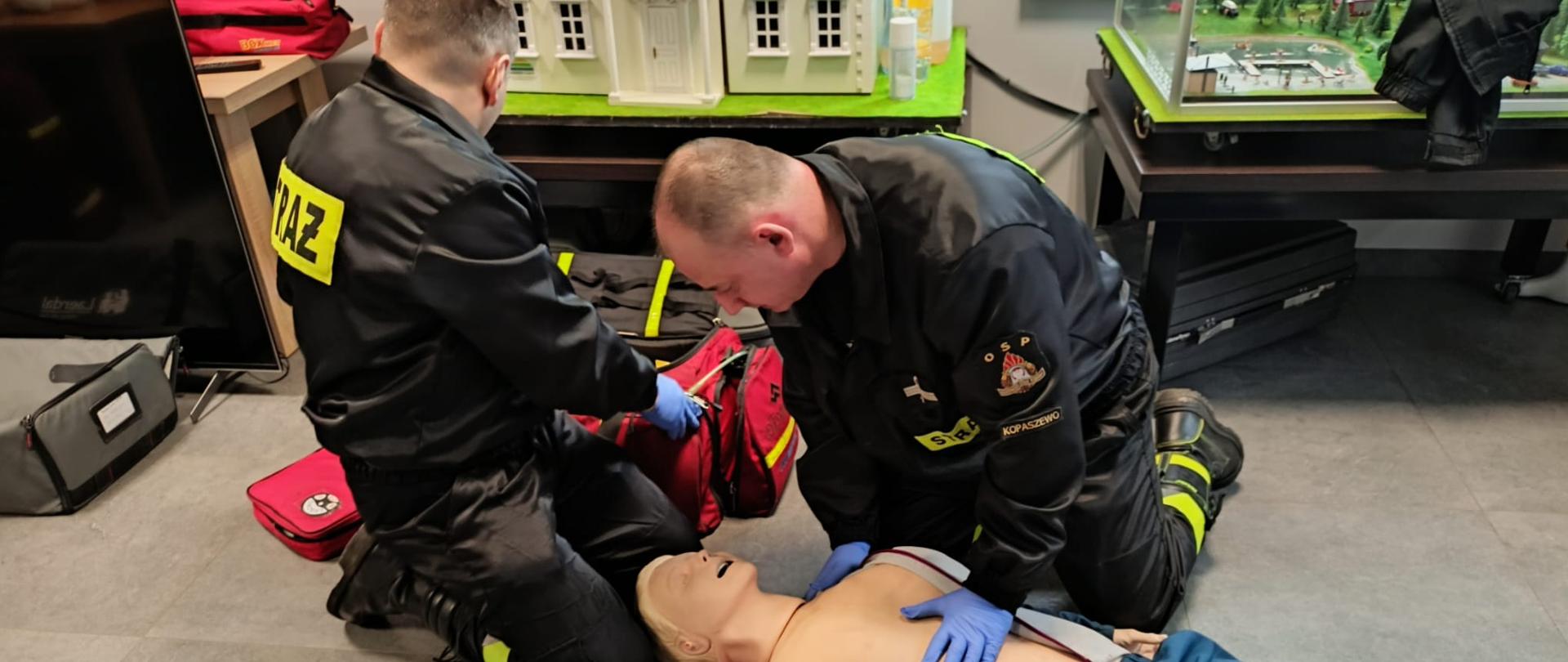 Strażacy podczas recertyfikacji uprawnień z kwalifikowanej pierwszej pomocy. Wykonują badanie osoby poszkodowanej i resuscytacji krążeniowo-oddechowej.