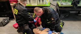 Strażacy podczas recertyfikacji uprawnień z kwalifikowanej pierwszej pomocy. Wykonują badanie osoby poszkodowanej i resuscytacji krążeniowo-oddechowej.