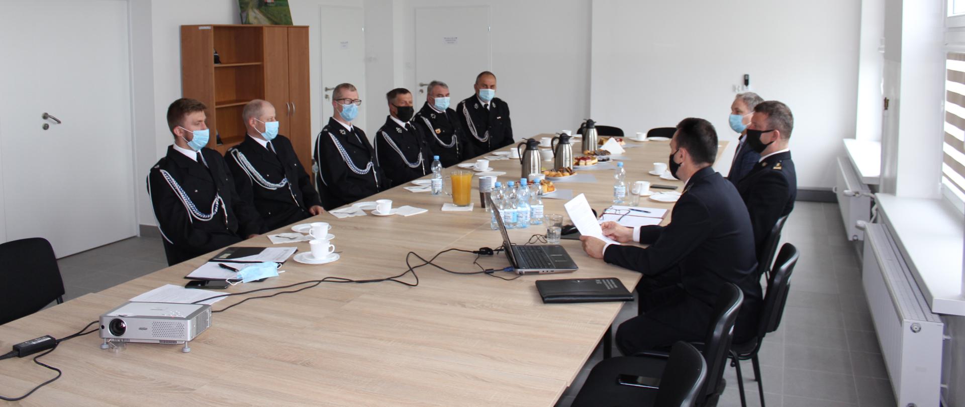 Na sali narad uczestnicy spotkania siedzą za stołami. Widoczni są Zastępca Komendanta Miejskiego PSP w Łomży, Naczelnik Wydziału Operacyjnego KM PSP w Łomży, wójt gminy Jedwabne oraz członkowie ochotniczych straży pożarnych.