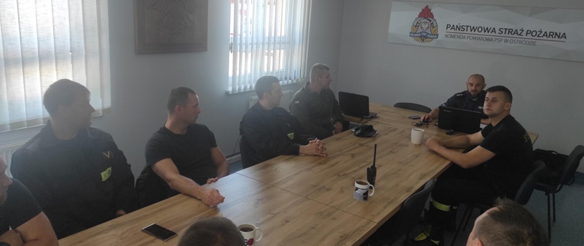Strażacy siedzą w sali konferencyjnej i słuchają wypowiedzi policjanta. 