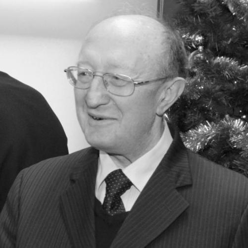 zdjęcie czarno białe przedstawia mężczyznę w okularach w garniturze w białej koszuli i z krawatem, w tle widać choinkę