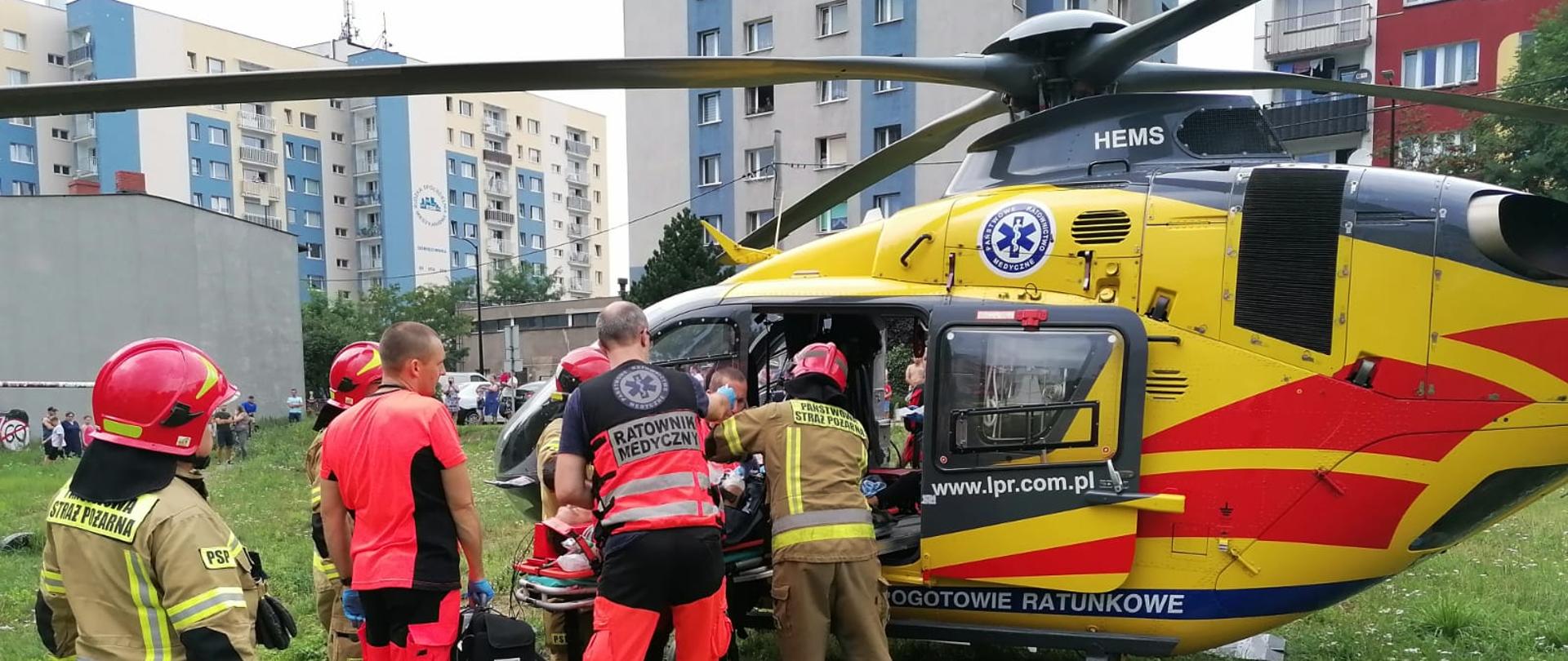 Zdjęcie przedstawia strażaków i ratowników medycznych podczas transportu osoby poszkodowanej do śmigłowca LPR.