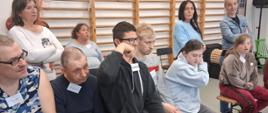 Uczestnicy spotkania, podnosząc dłoń, zadają pytania prowadzącemu