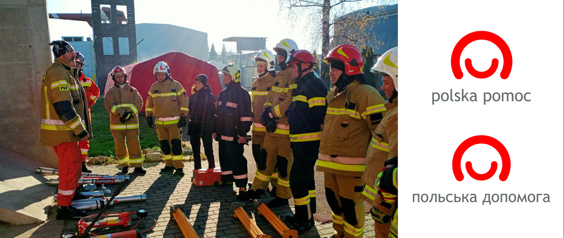 Grupa ratowników słucha wykładu prowadzącego zajęcia, przed nimi rozłożone są na ziemi elementy sprzętu ratowniczego. Po prawo logo polskiej pomocy w języku polskim i ukraińskim