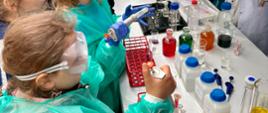 Dzieci przebrane w fartuchy testują sprzęt laboratoryjny na stoisku WSSE w Rzeszowie