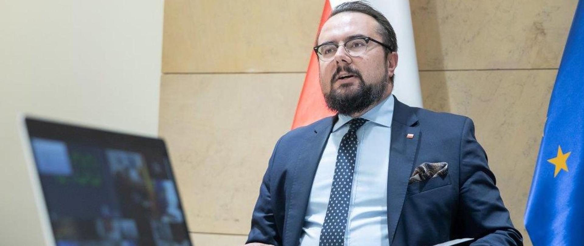 mężczyzna w garniturze siedzi na tle flagi Polski i UE