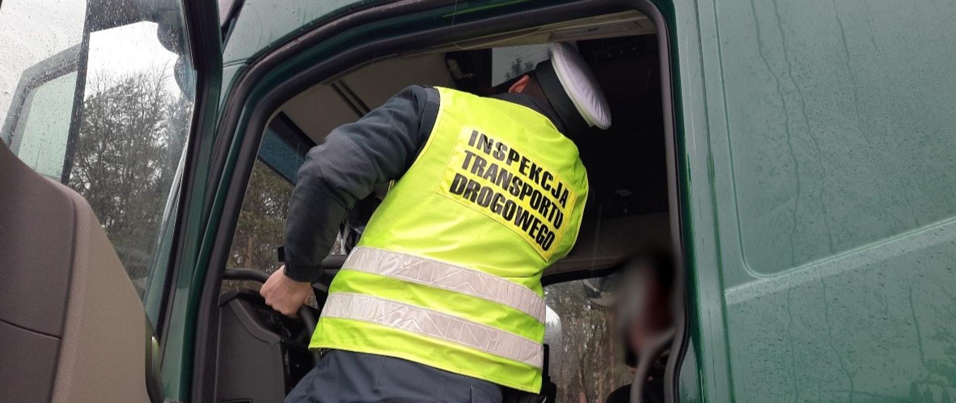 Umundurowany funkcjonariusze Inspekcji Transportu Drogowego stoi w wejściu do kabiny ciężarówki i pobiera dane z tachografu cyfrowego. (Ilustracja: archiwum GITD)