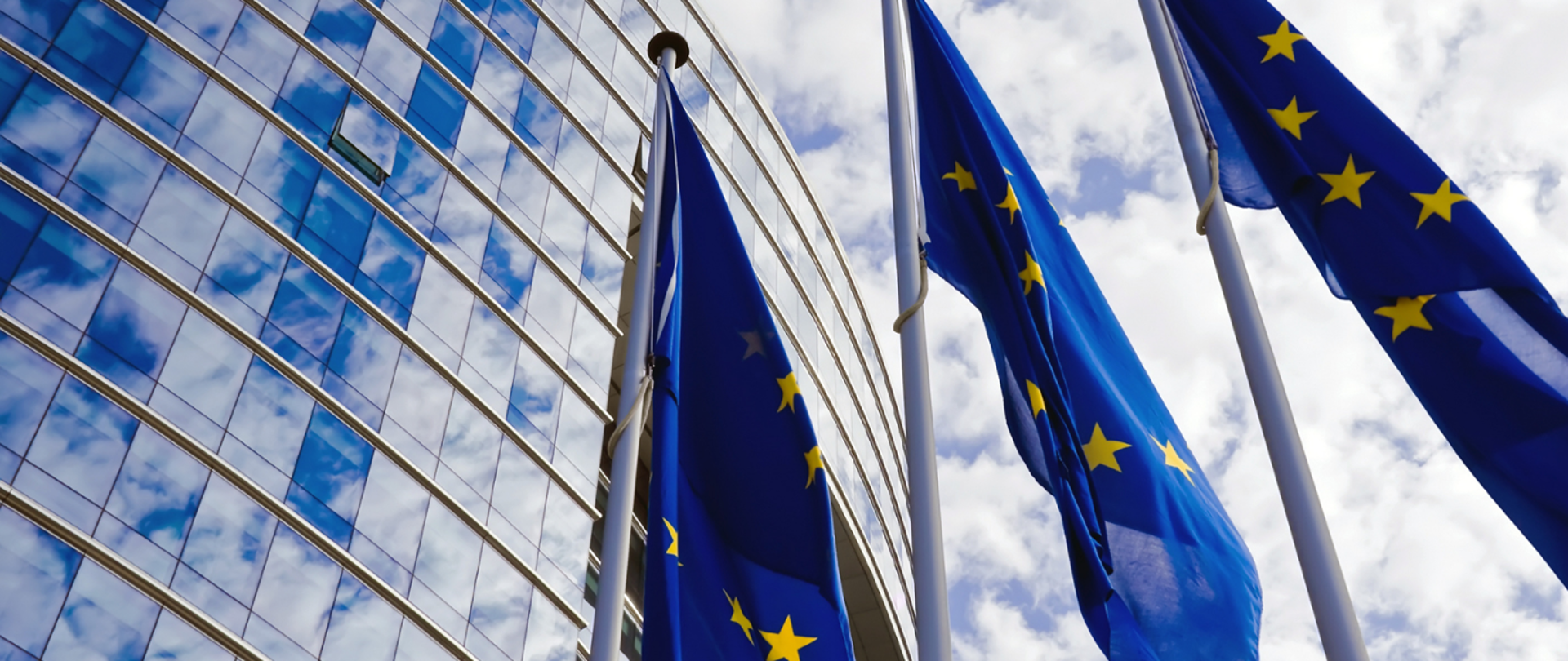Zdjęcie trzech flag UE, w tle niebo.