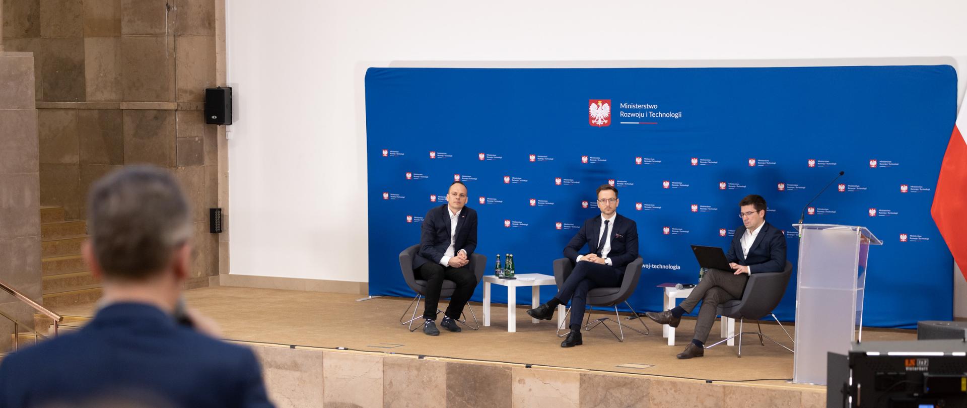 Minister Waldemar Buda podczas debaty poświęconej waloryzacji wynagrodzeń wykonawców zamówień publicznych. Na zdjęciu widać scenę i uczestników debaty. 