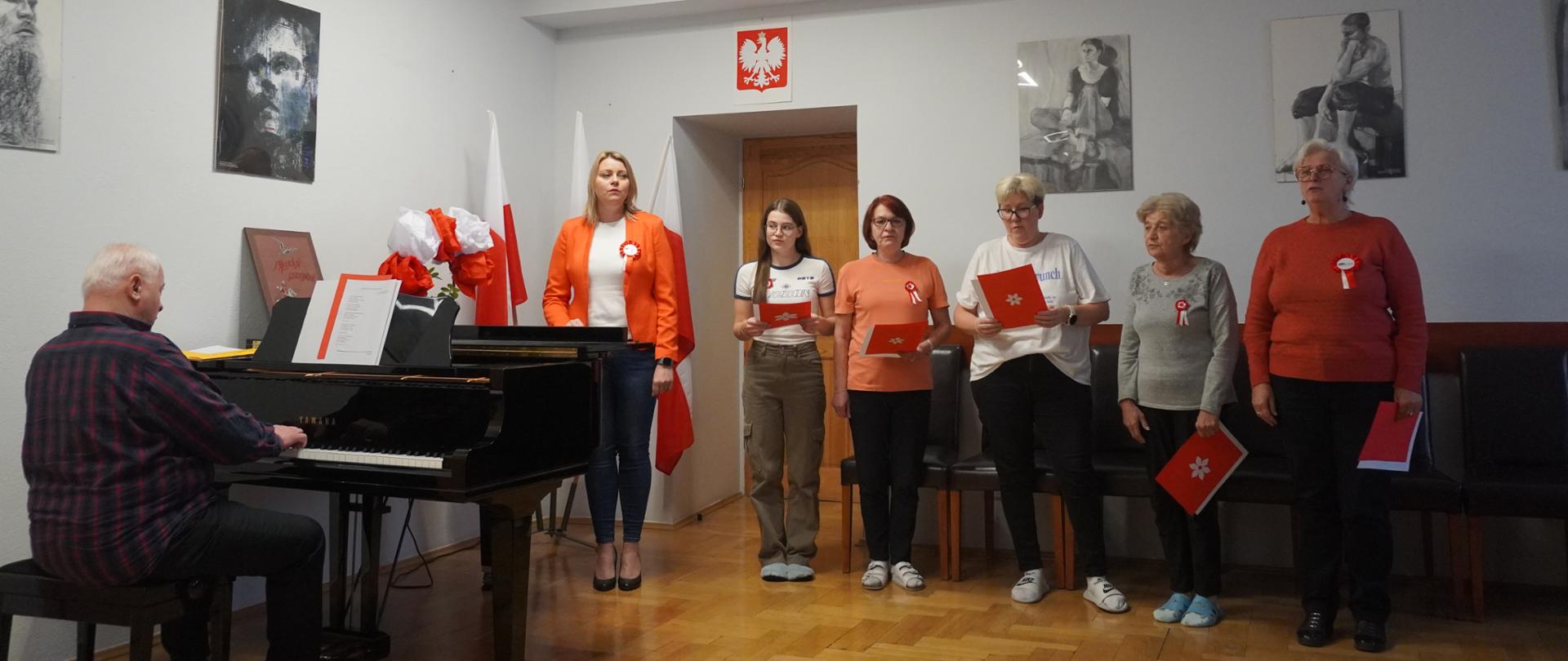 Pani Dyrektor, pracownicy i wychowanka śpiewają hymn przy akompaniamencie fortepianu.