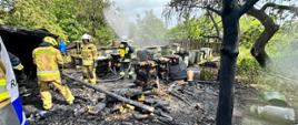Strażacy pracują na zgliszczach budynku gospodarczego. Po środku widać nadpalone ule.